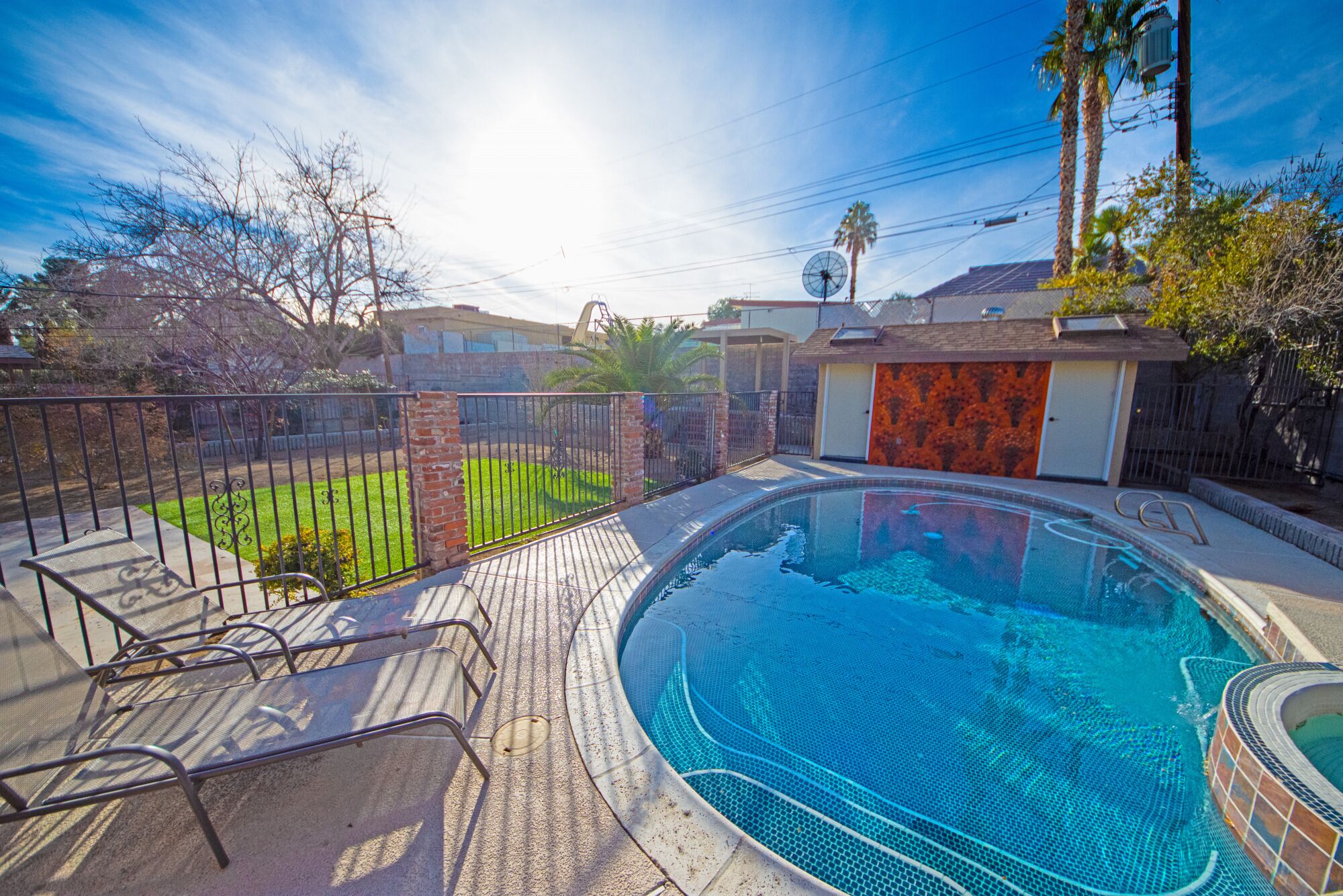 A swimming pool with a tiled edge, surrounded by a brick wall and a metal fence.