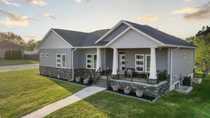 A two-story house with a stone foundation, a front porch, and a small patio area. - Modern comfort, small town charm. Room for 
all to visit, rest retreat or create (Center Point)