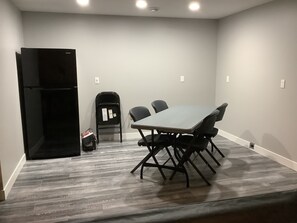 Una sala conferenze con un tavolo e sedie, una sedia pieghevole nera, un frigorifero nero e un pavimento rivestito di moquette grigia.