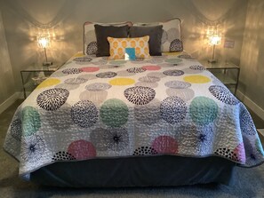 Un letto con una coperta a motivi, due abat-jour e un comodino con un ripiano in vetro.