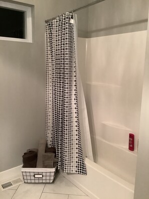 Un bagno con una tenda da doccia a pois, una vasca da bagno bianca e un piccolo oblò sopra la doccia.