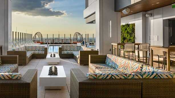 A rooftop lounge with wicker furniture, a central fire feature, and a view of the city skyline. - 1BD Deluxe/Atlanta Margaritaville - Downtown w/Rooftop Pool and Pool Bar! (Atlanta)