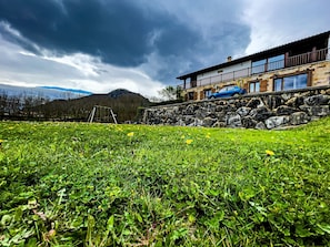 A stone building with a balcony, surrounded by a grassy field with yellow flowers.