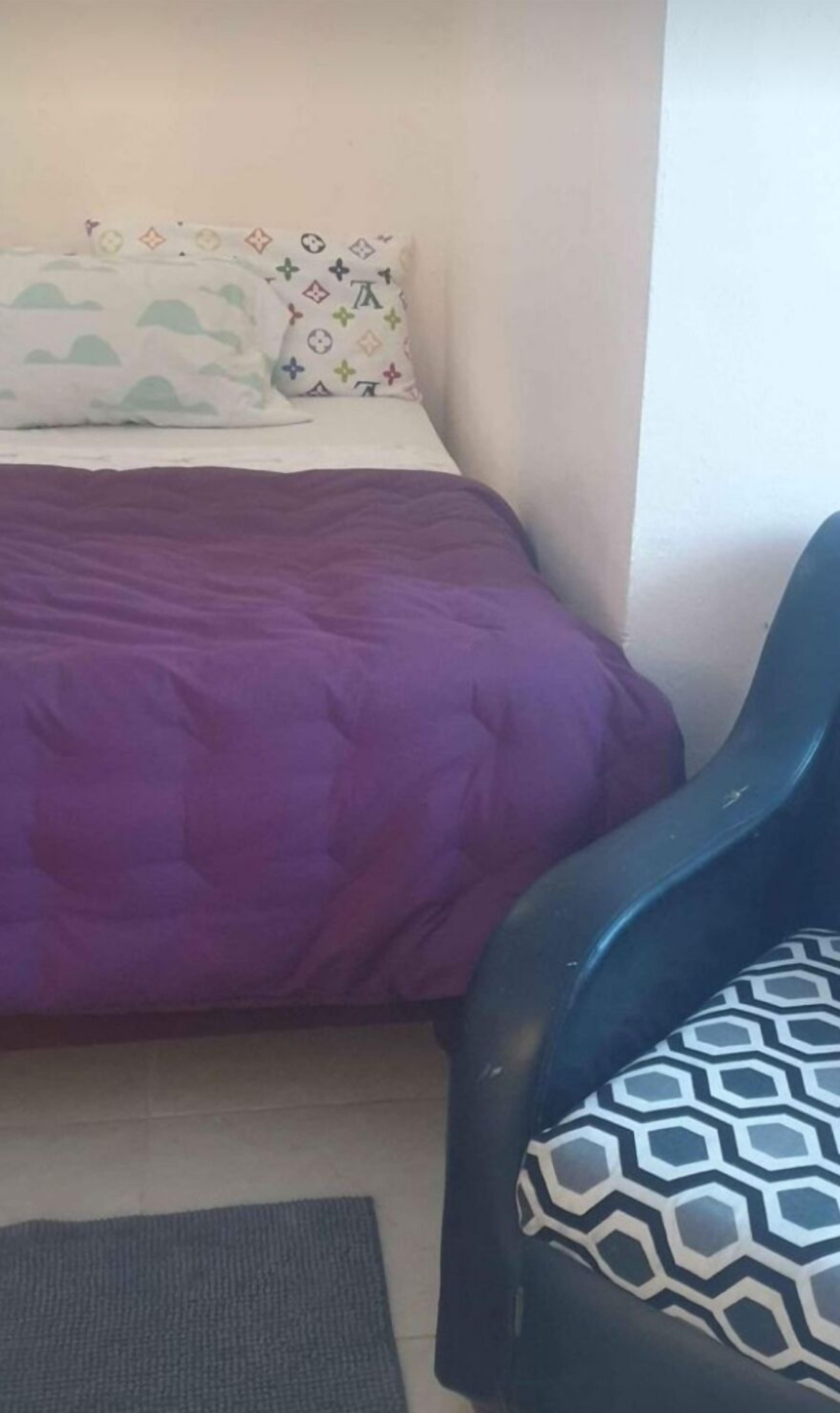 Ein kleiner, schlichter Raum mit einem Bett, einem Sessel und einem Teppich.