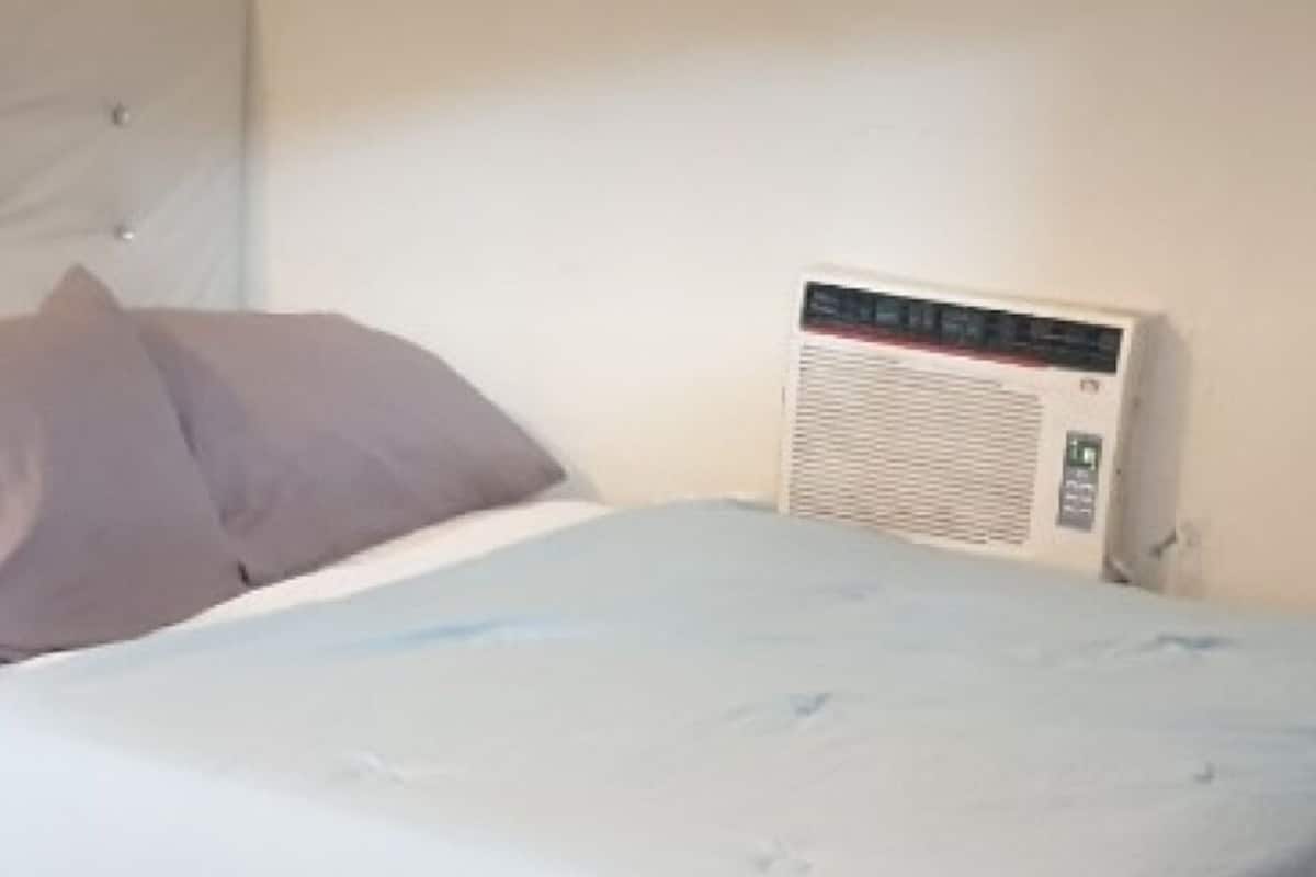 A bed with a light blue bedspread, a red rug, and a white wall.