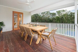 A wooden deck with a table and chairs, a ceiling fan, and a view of trees.