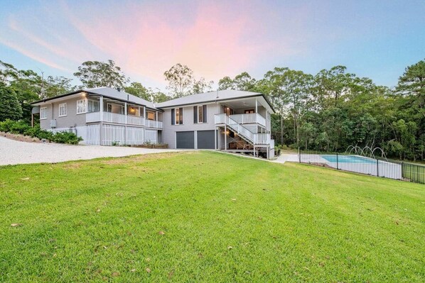 A two-story house with a large front yard, a swimming pool, and a staircase leading to the upper floor.