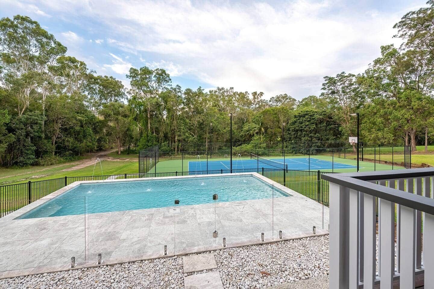 Ein Schwimmbad mit einem Basketballplatz im Hintergrund, umgeben von Bäumen.