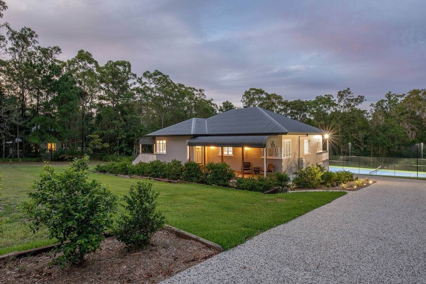 A modern house with a covered porch, a well-maintained lawn, and a tennis court.