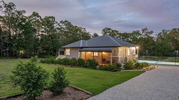 A modern house with a covered porch, a well-maintained lawn, and a tennis court.