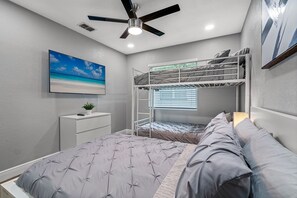 A bedroom with a bunk bed, a bedside table with a lamp, a ceiling fan, and a painting of a beach. - Great Duplex, 2 Kitchens, Sleeps 12 | 5 Min to Busch Gardens, Tampa (Tampa)