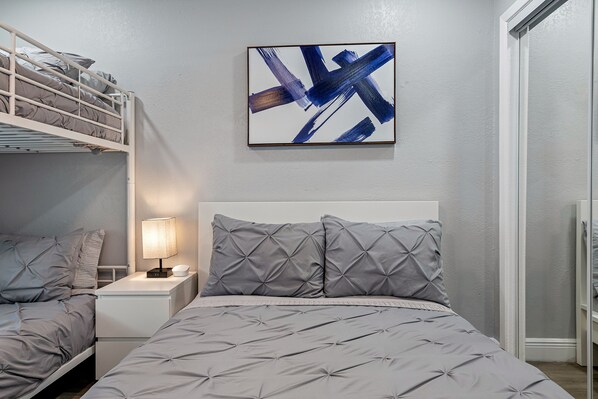 Une chambre avec un lit superposé, une table de chevet avec une lampe et un tableau abstrait encadré accroché au mur.