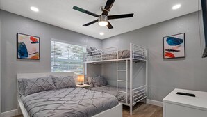Een slaapkamer met stapelbedden, een plafondventilator, een nachtkastje met een lamp en kunstwerken aan de muur.