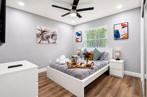A modern bedroom with a bed, bedside tables, a ceiling fan, artwork, and a window with blinds. - Great Duplex, 2 Kitchens, Sleeps 12 | 5 Min to Busch Gardens, Tampa (Tampa)