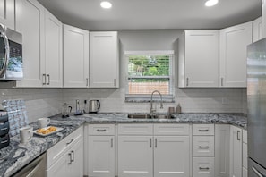 A modern kitchen with white cabinets, a granite countertop, a window with blinds, and a stainless steel sink. - Entire Duplex, 2 Kitchens, Sleeps 12 | 5 Min to Busch Gardens, Tampa (Tampa)