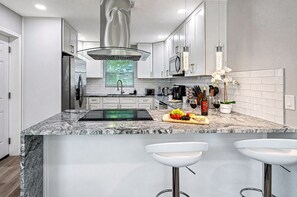 Une cuisine moderne dotée d’un îlot central, d’appareils électroménagers en acier inoxydable et d’un revêtement mural décoratif à motifs géométriques.
