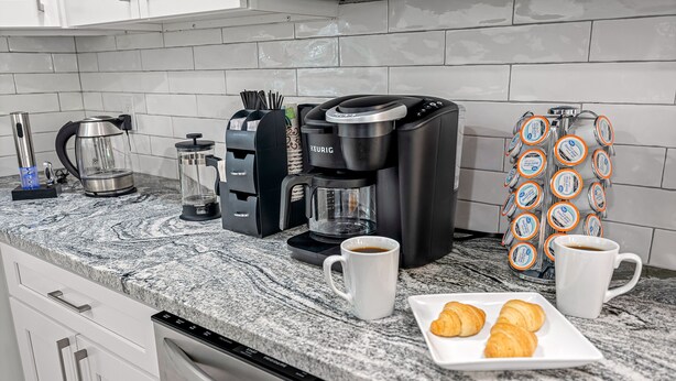 Een keuken met een koffiezetapparaat, een waterkoker, een koffiekan, een koffiemachine, een melkopschuimer en een koffiepadapparaat.