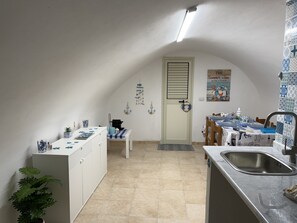 Eine kleine Küche mit Spüle, einem Esstisch mit blauer Tischdecke und einem weißen Schrank.