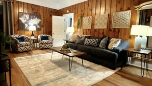 A living room with a wooden floor, a sofa, two armchairs, a coffee table, and a rug.