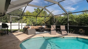 A covered outdoor area with a pool, seating, and a grill.