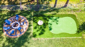 A circular seating area with a fire pit, surrounded by a chain-link fence, and a putting green with a golf ball.