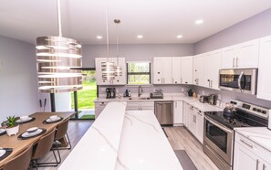 Une cuisine moderne avec des meubles blancs, des appareils en acier inoxydable et un grand îlot central doté de sièges.