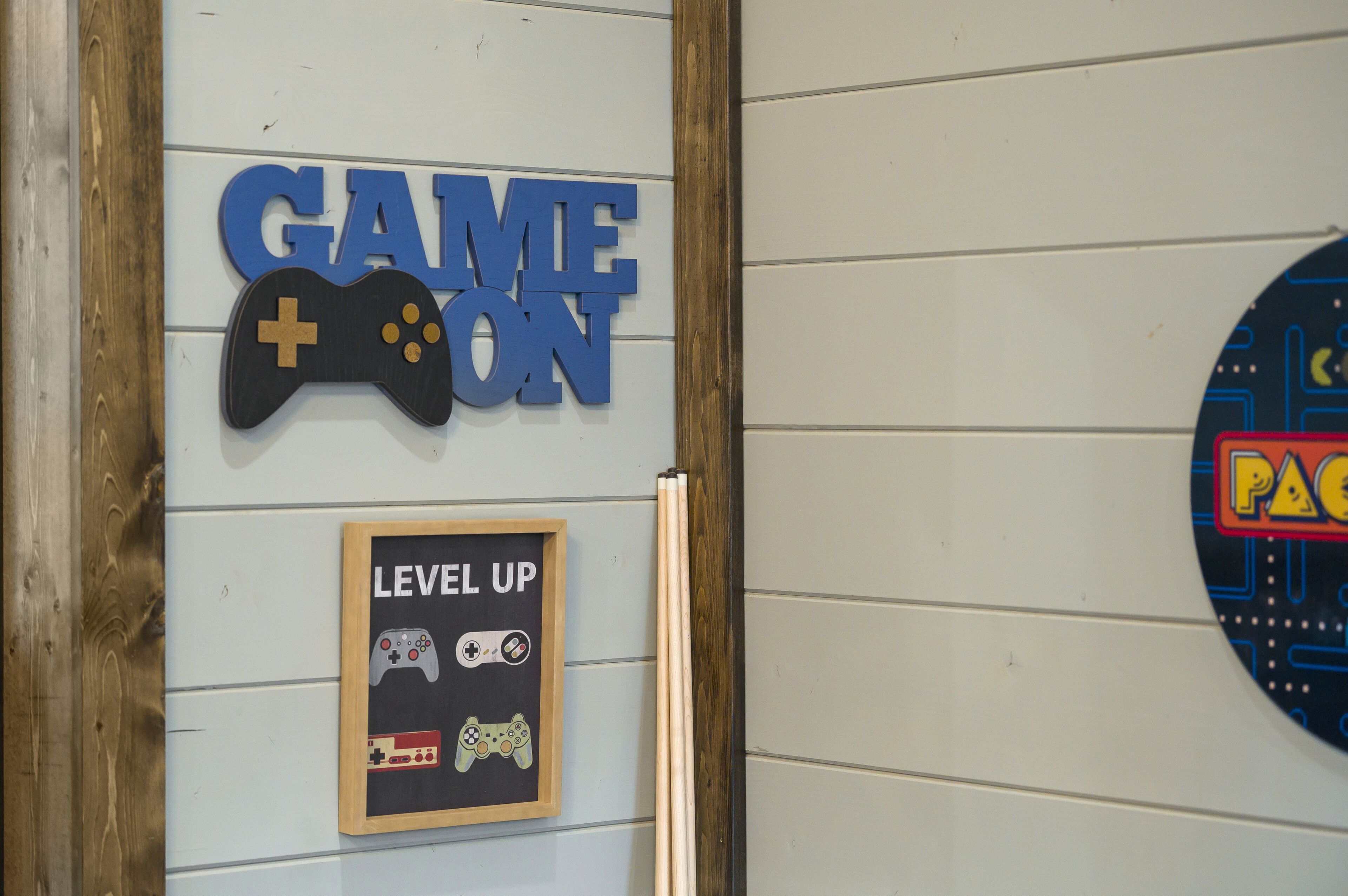 Una pared con un letrero que dice “GAME ON” y un cartel enmarcado con “LEVEL UP” y gráficos de controles de videojuegos.