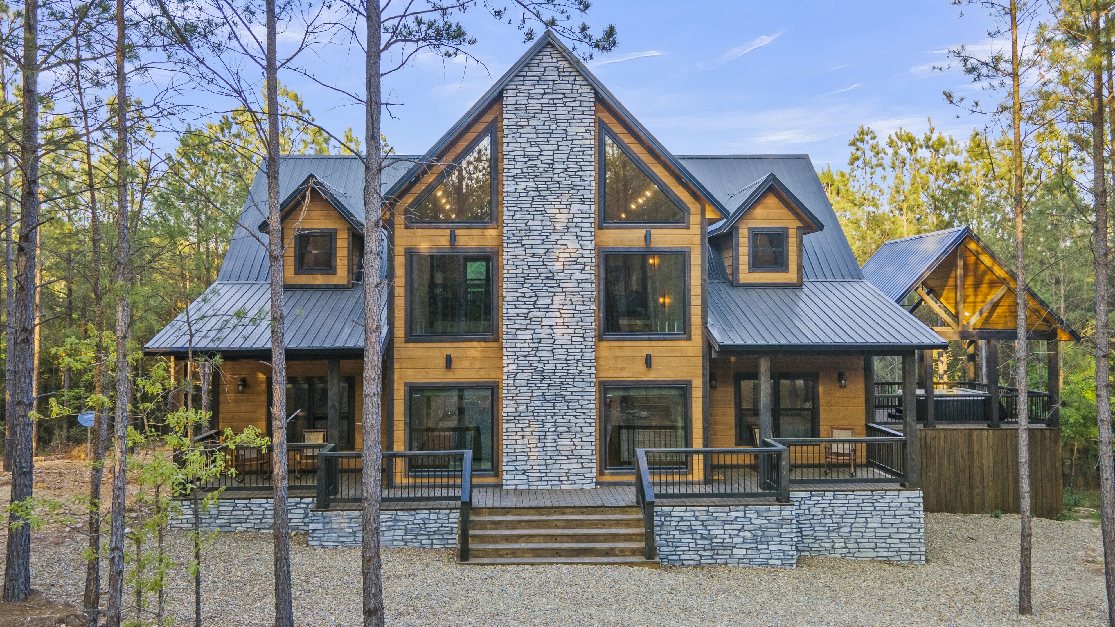 Une grande cabane moderne en rondins de bois, dotée d’une façade en pierre, de nombreuses fenêtres et d’un porche.