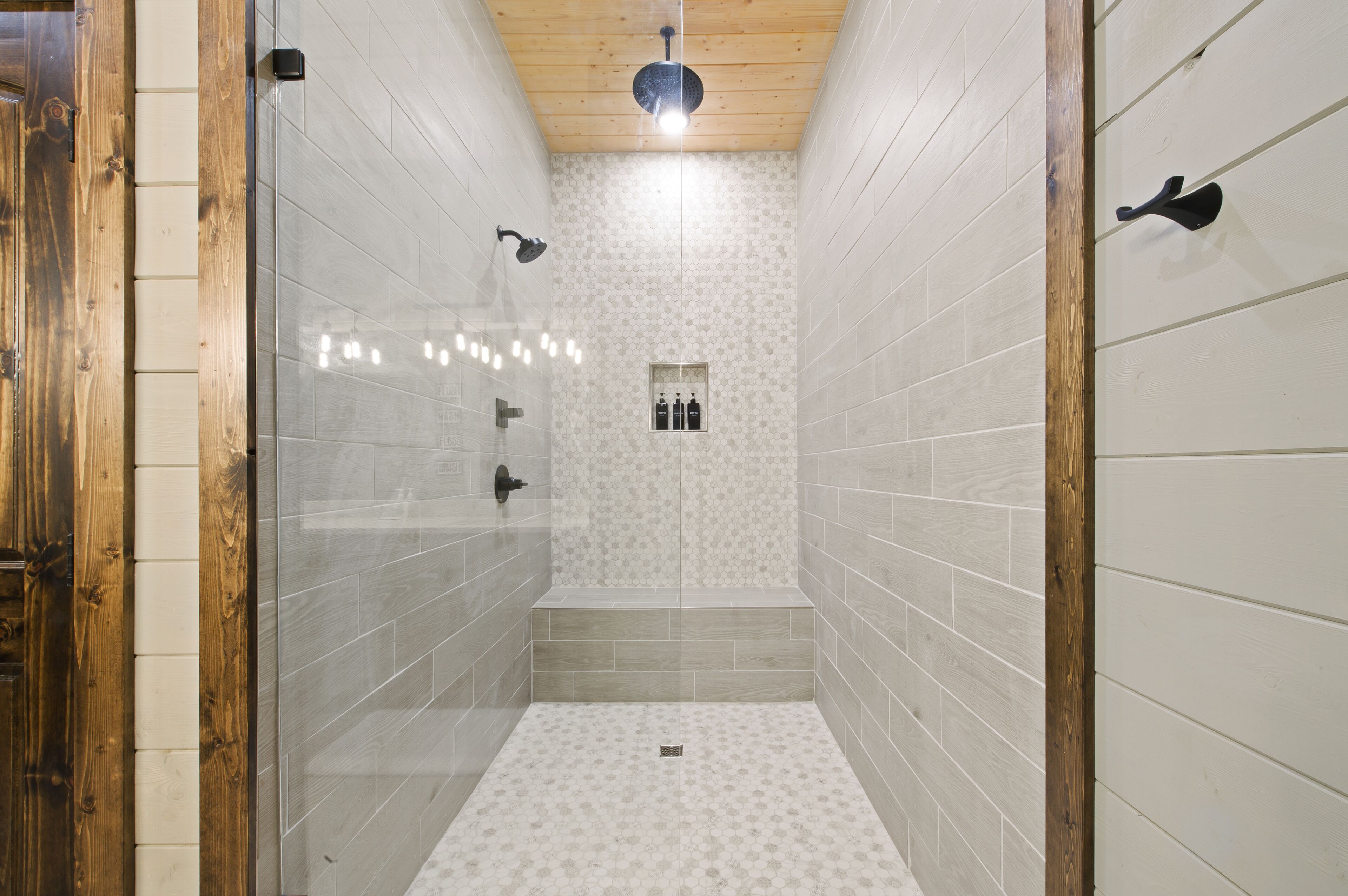A narrow shower area with tiled walls, a wooden ceiling, and a bench.
