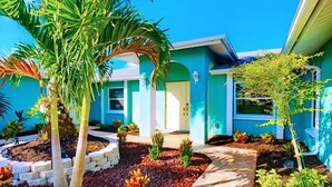 A blue house with a garden, a palm tree, and a pathway leading to the door. - 30% Disc-2 Kg Mstrs, Golf, Fishing, BBQ, Pool, Spa (Cape Coral)