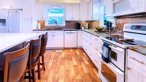 A modern kitchen with white cabinetry, a wooden floor, and a large island with bar stools. - 30% Disc-2 Kg Mstrs, Golf, Fishing, BBQ, Pool, Spa (Cape Coral)