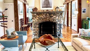 A spacious living room with a stone fireplace, a dog lying on the floor, and a high ceiling. - Secluded, Private Vacation Beach Home on Chappaquiddick Island, Walk To Beach. (Edgartown)