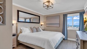 A hotel room with a large bed, a desk with a computer, a window with a beach view, and a ceiling light fixture. - Panoramic oceanfront views, ground floor luxury renovation next to Ocean Annie’s (Myrtle Beach)