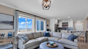A modern living room with a sectional sofa, a coffee table, and a view of the ocean through large windows. - Panoramic oceanfront views, ground floor luxury renovation next to Ocean Annie’s (Myrtle Beach)