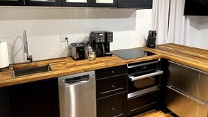 A modern kitchen with black cabinets, a wooden countertop, a dishwasher, an oven, and a coffee maker. - Spacious West End Penthouse | Great for Groups (Portland)