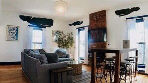 A modern living room with a grey sofa, a coffee table, and a brick fireplace. There are two bar stools and a dining table. - Spacious West End Penthouse | Great for Groups (Portland)