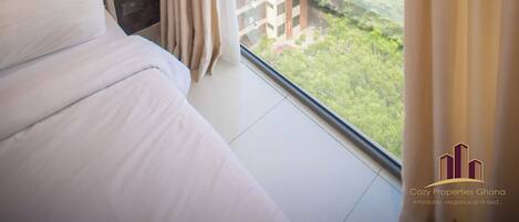A bedroom with a large window, a bed, and a nightstand.