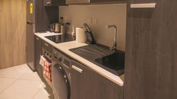 A modern kitchen with dark wood cabinets, a stainless steel microwave, a built-in oven, a sink with a faucet, and a washing machine.