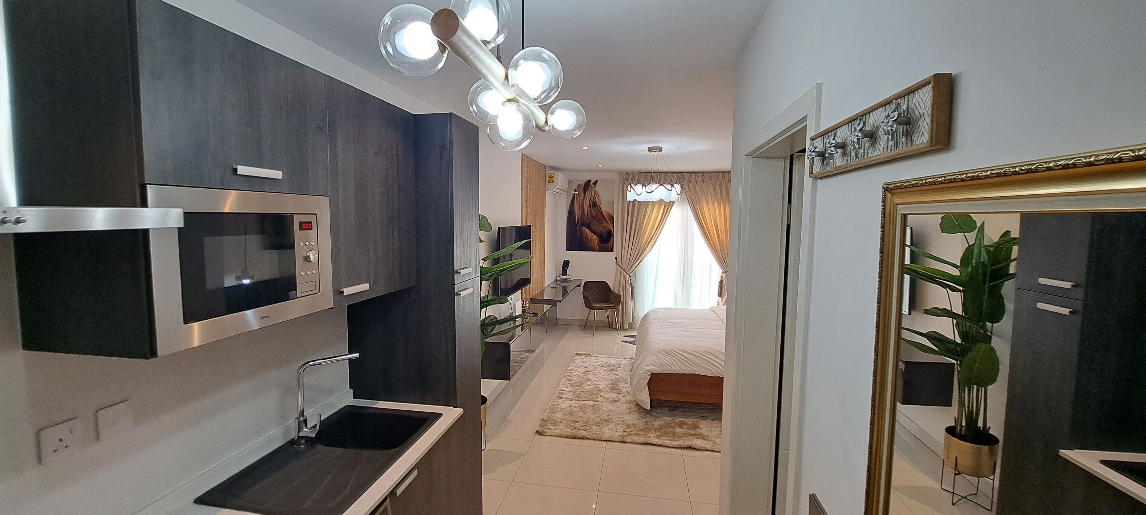 A modern kitchen with built-in appliances, a dining area with a chair, and a bedroom with a bed and curtains.