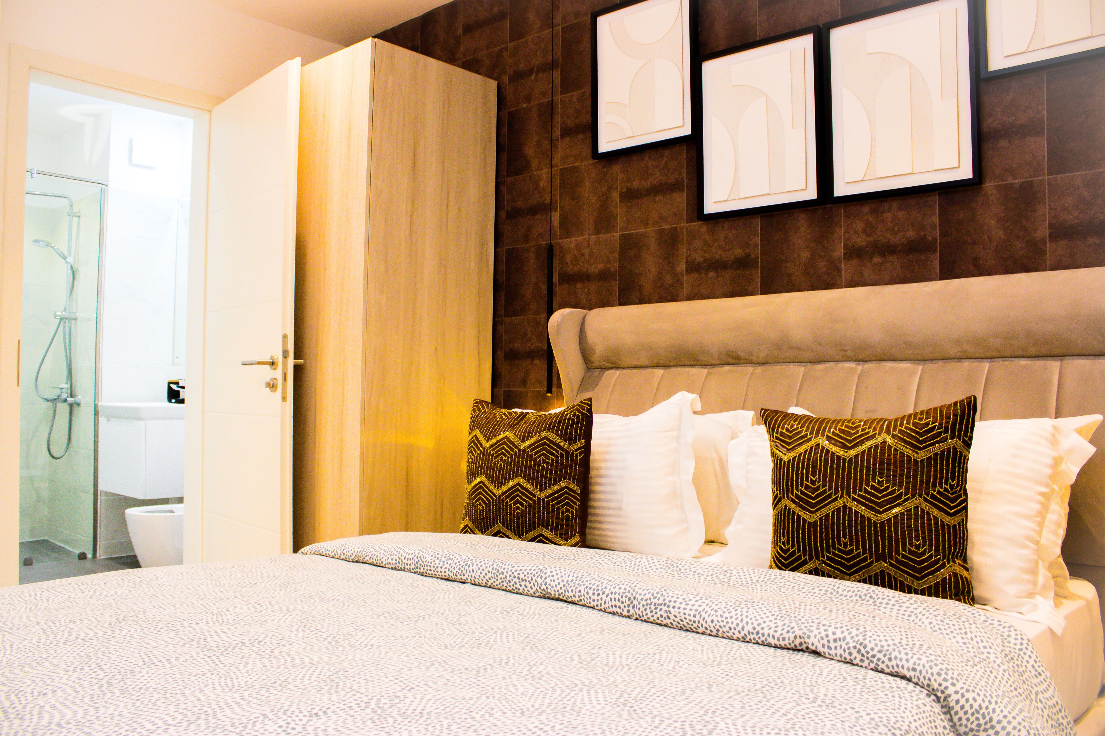 A hotel room with a large bed, a wardrobe, a shower area, and framed artwork on the wall.