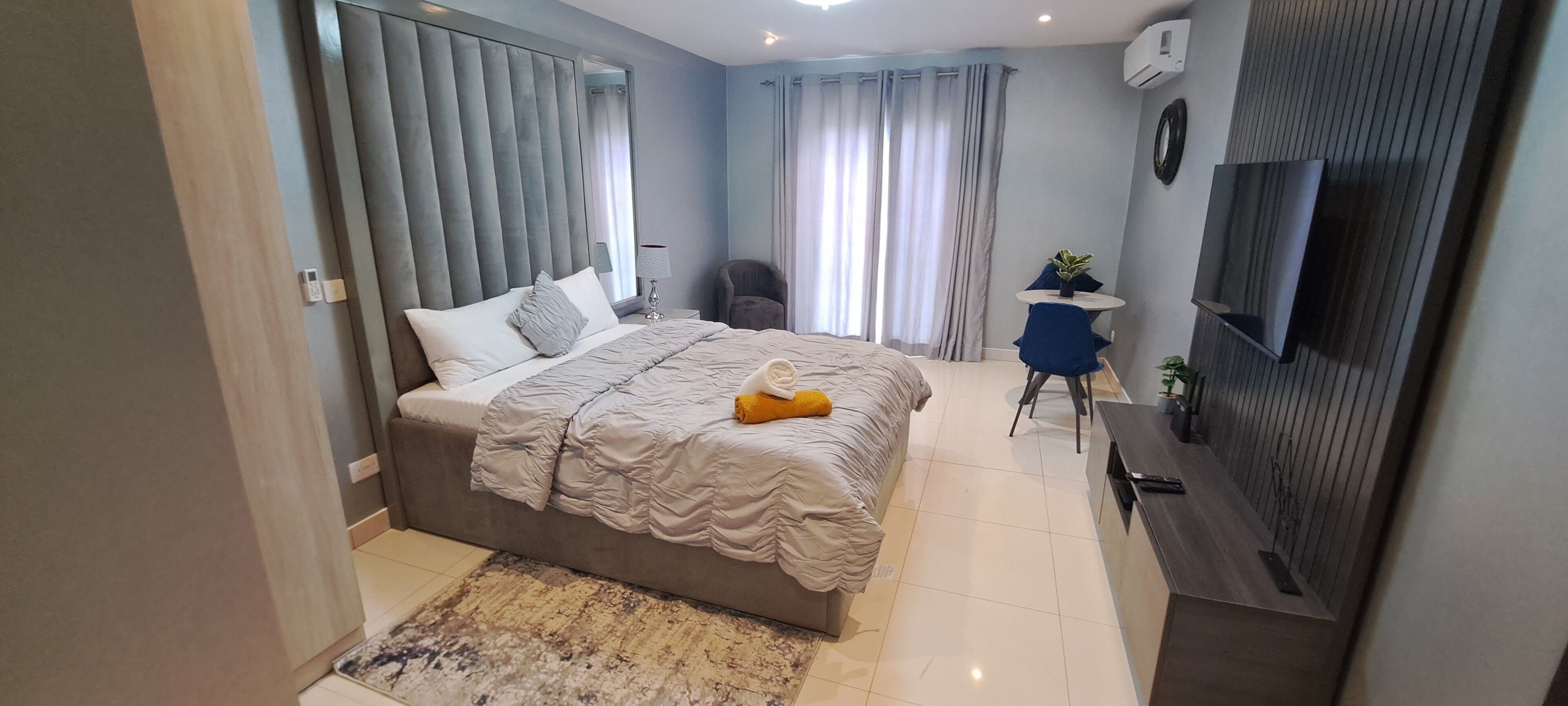 A modern bedroom with a large bed, a small desk, a chair, and a TV mounted on the wall.