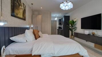 Une chambre moderne avec un grand lit, un téléviseur à écran plat, un coin repas et une cuisine en arrière-plan.