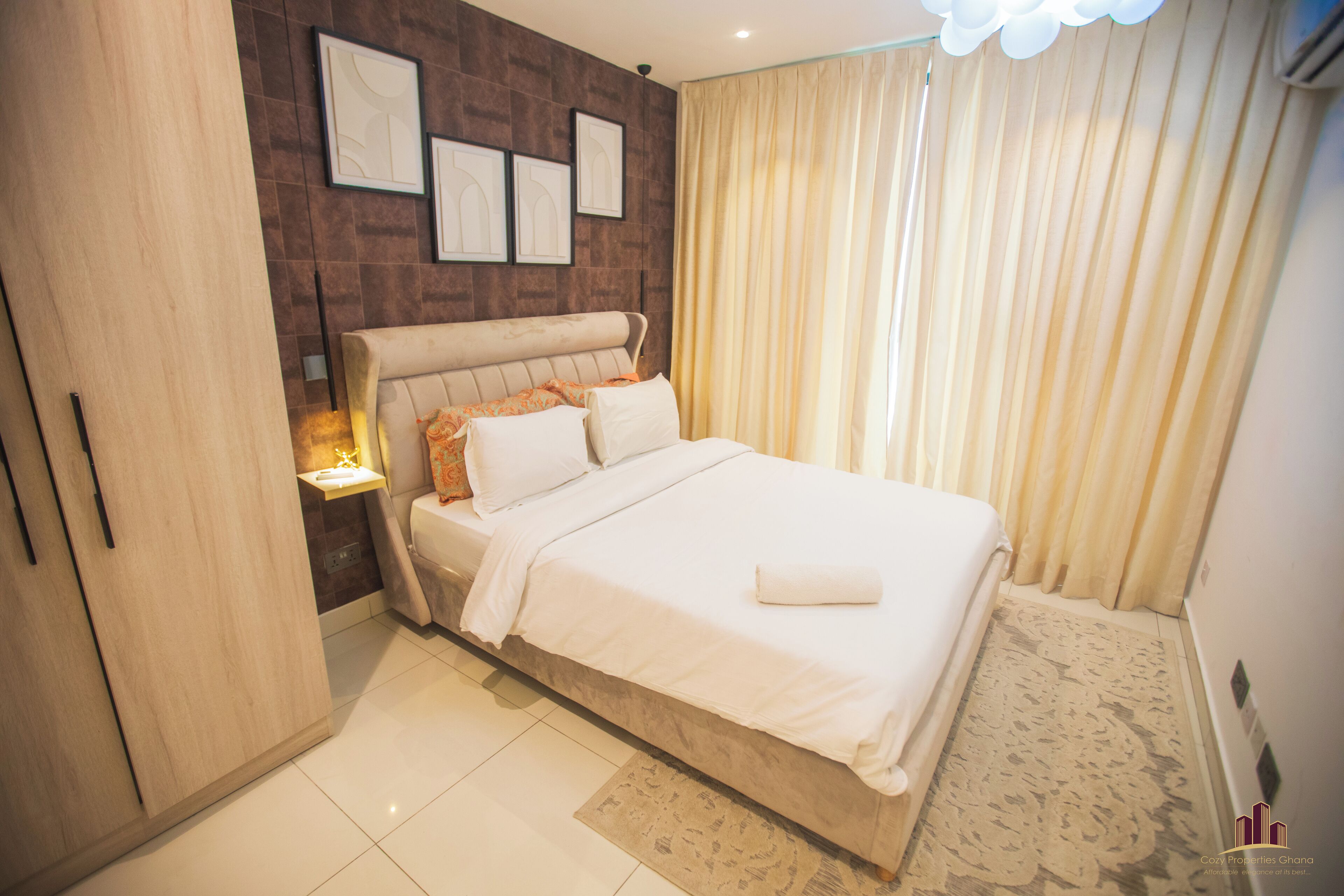 A bedroom with a bed, a nightstand, a wardrobe, and a wall with framed pictures.