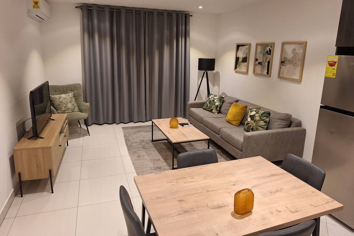 A modern living room with a sofa, coffee table, TV, and a dining area with chairs and a table.