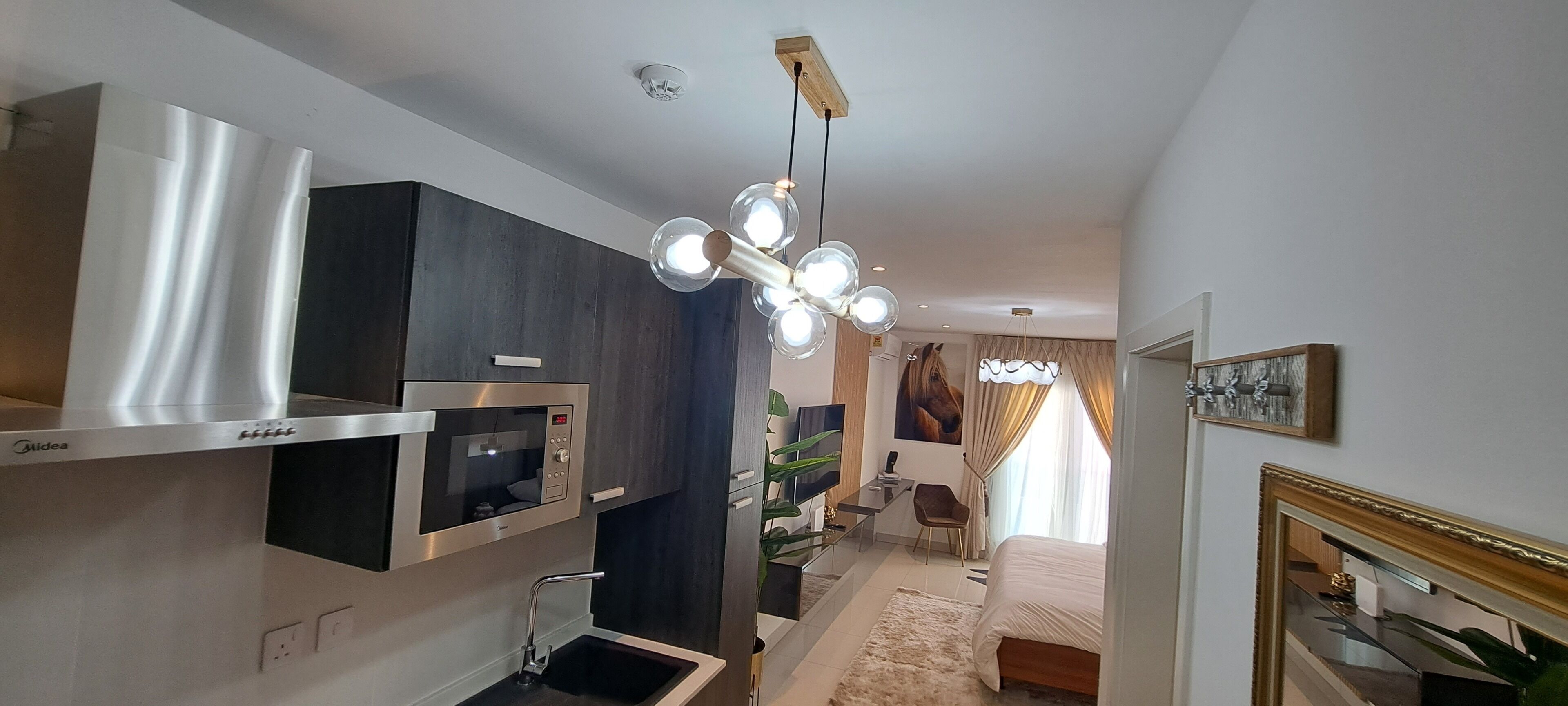A modern hotel room with a kitchenette, a large bed, a TV, and a chandelier.