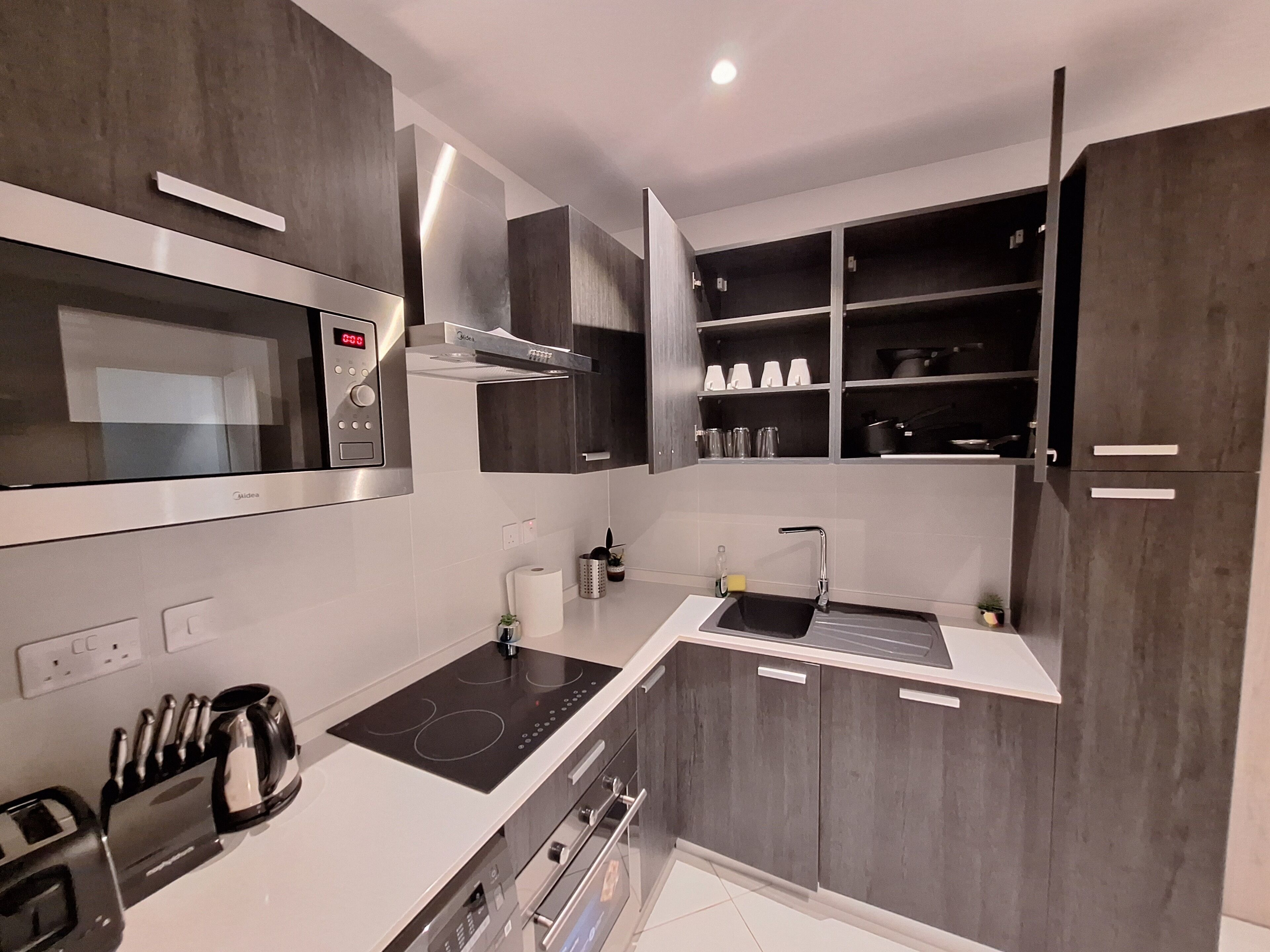 Een moderne keuken met een ingebouwde magnetron, fornuis en oven. Er is een spoelbak met een kraan, en kasten met servies en glaswerk.