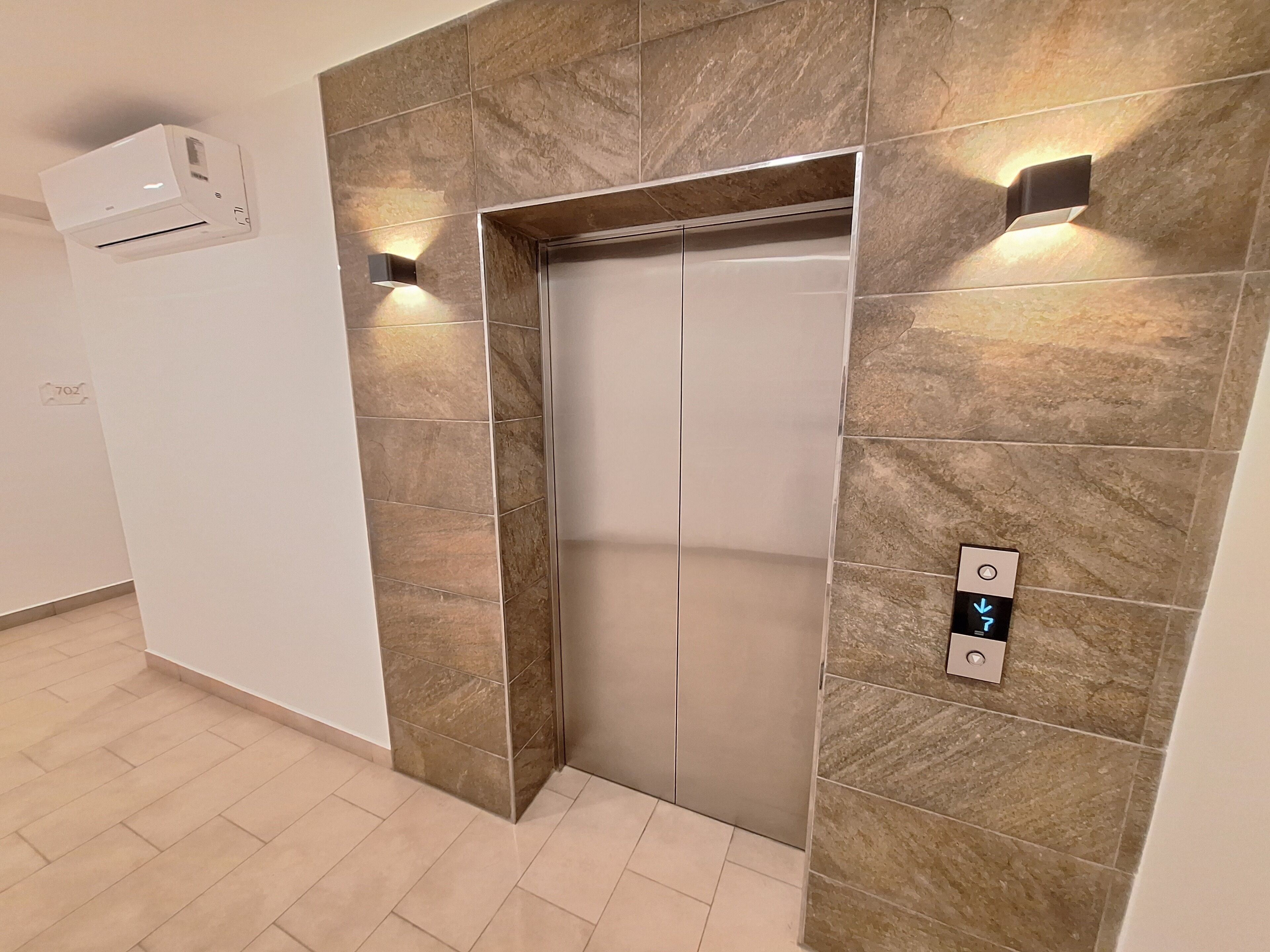 An elevator with a modern design, featuring a metallic finish and a control panel with directional arrows.