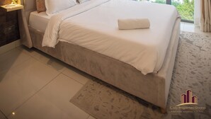 A modern bedroom with a large bed, a city view, and a unique ceiling light fixture. - The Lennox Abode (Accra)