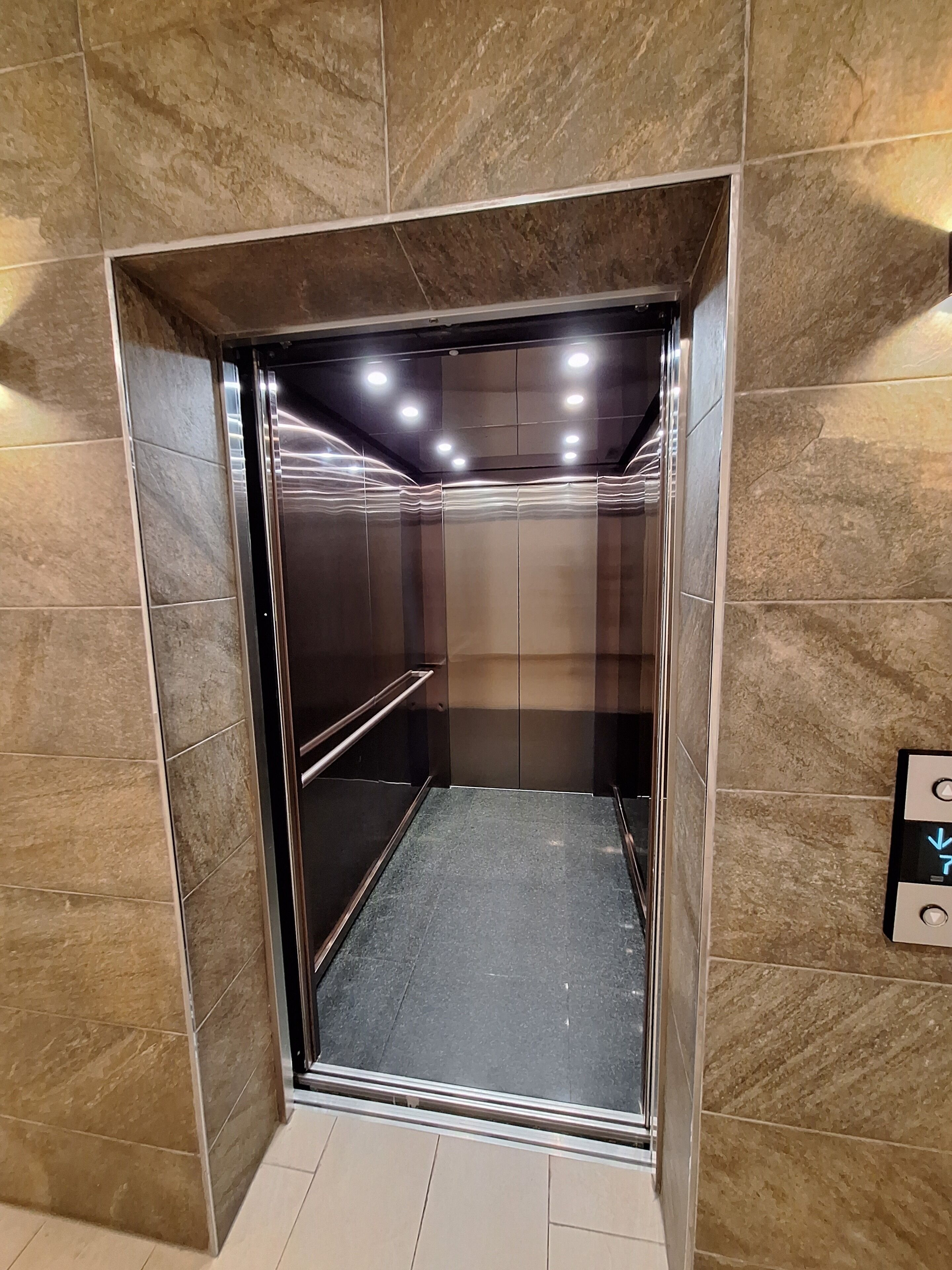 Een lift met een metalen binnenkant, een handgreep en een bedieningspaneel met pijlen.