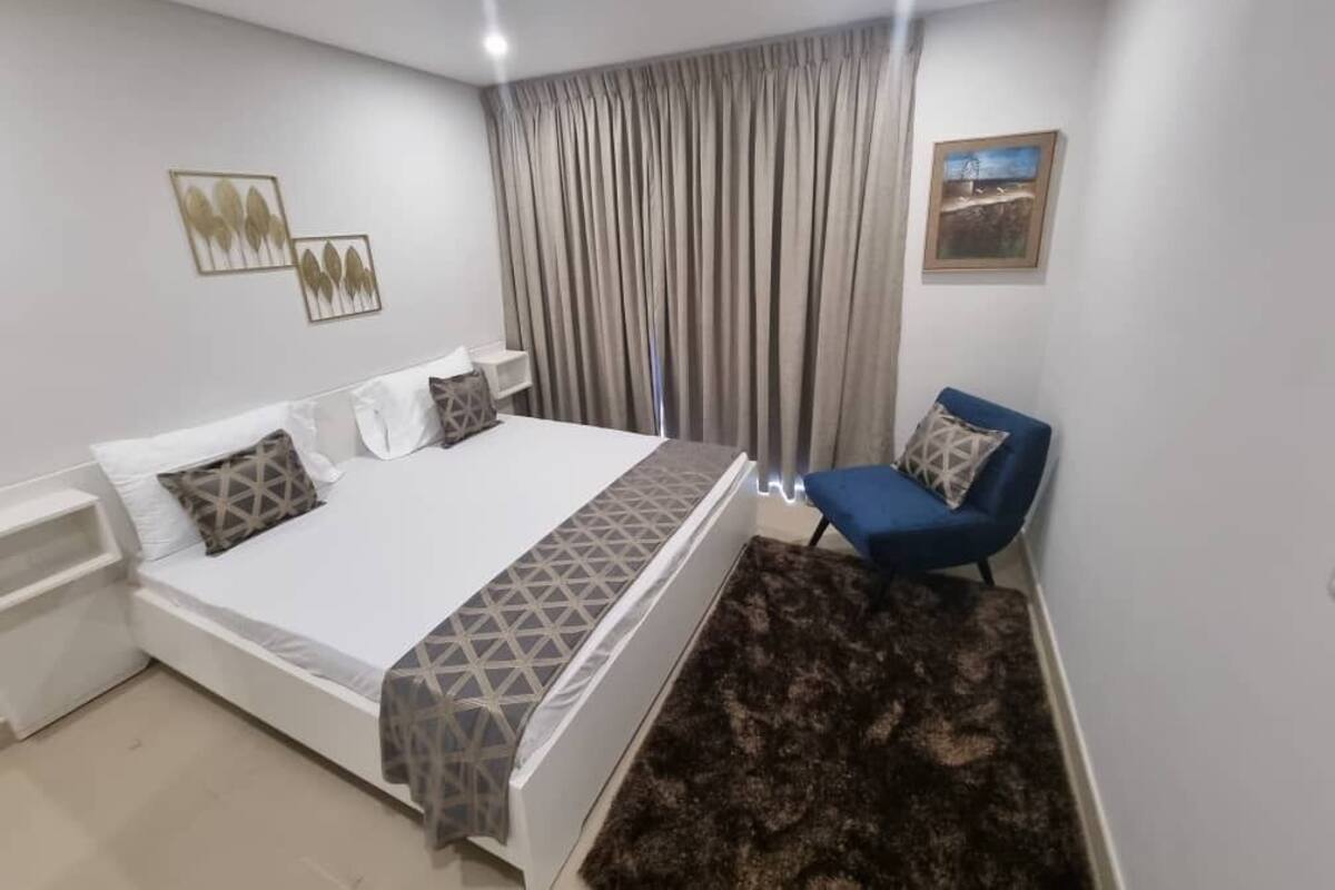 Une chambre à coucher avec un lit, une chaise, une table de chevet, un tapis et un tableau au mur.